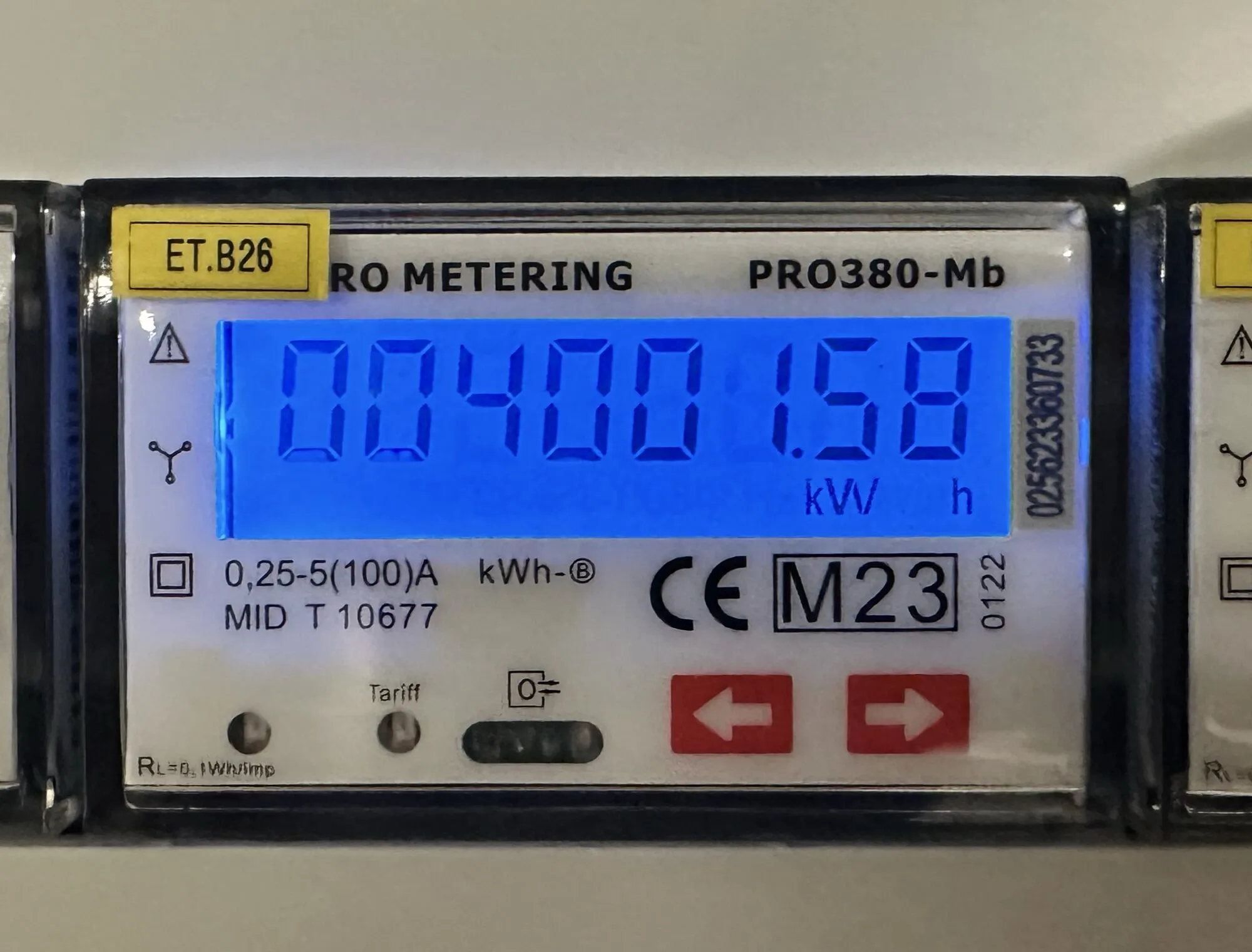 Elektroměr modře podsvícený displej se stavem 004001.58 kWh, žlutý štítek ET.B26 vlevo nahoře a dvě červená tlačítka se šipkami dole.