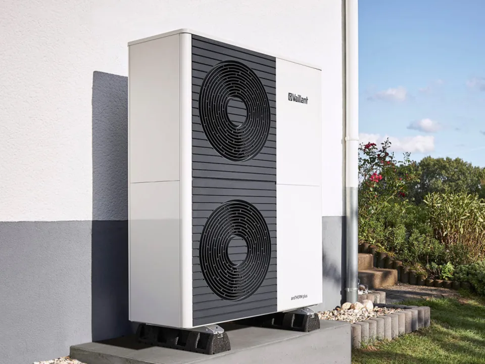 Venkovní jednotka tepelného čerpadla Vaillant aroTHERM plus u fasády domu — vysoká bílá skříň s tmavým lamelovým výměníkem a dvěma kruhovými ventilátory nad sebou